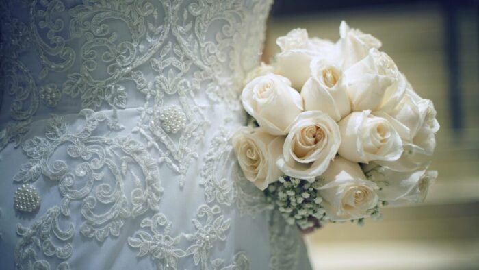 Detalle del bordado del vestido de novia junto al ramo de rosas.
